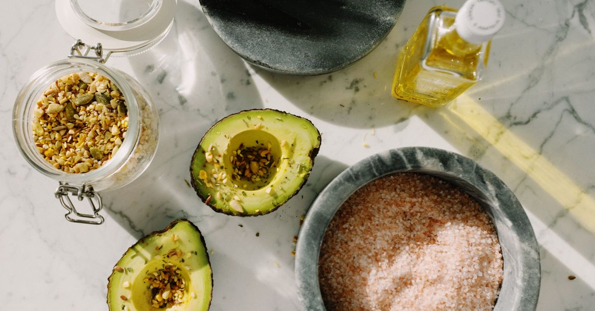top view of tasty halved avocado sprinkled with various seeds placed near pink salt with seed mixtur